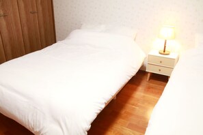 Una cama bien hecha con edredón blanco y almohadas, un armario de madera y una mesita de noche con una lámpara.
