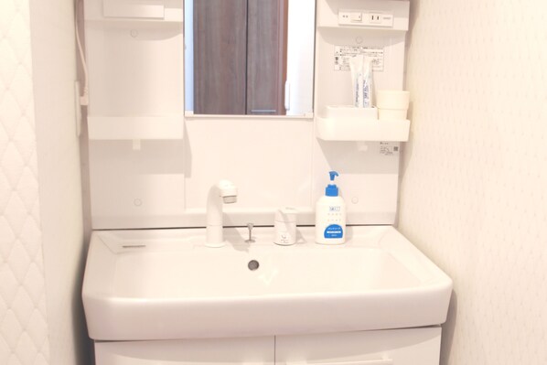 Een wit badkamermeubel met een spiegel erboven, een raam met houten jaloezieën en een klein plankje met toiletartikelen.