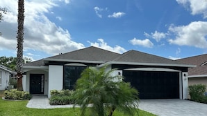 Een modern huis met twee verdiepingen, een garage, een verzorgd gazon en een palmboom.