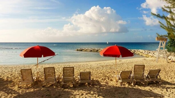 A beach with two red umbrellas and wooden lounge chairs facing the ocean. - Cozy & Safe Studio Apt Free Beach Access (Montego Bay)