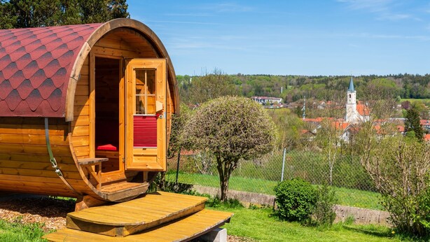 Una cabaña de madera con techo rojo, puerta de madera y un pequeño porche.