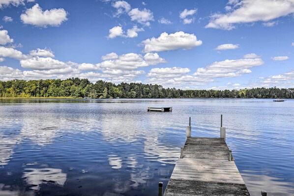 A calm lake with a wooden dock extending into the water, surrounded by dense forest.