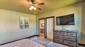A bedroom with a bed, a dresser, a ceiling fan, a painting, and a TV on the wall.
