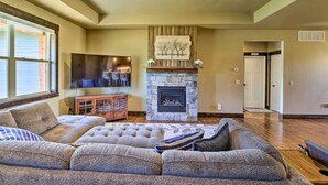 A living room with a stone fireplace, a large sectional sofa, and a television on a wooden cabinet.