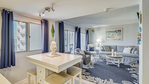 A modern living room with a dining area, a sofa set, and a large window with curtains. - Steps to Shore! PCB Resort Condo w/ Balcony (Panama City Beach)