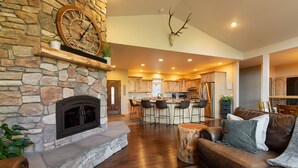 A spacious living area with a stone fireplace, leather sofa, and a kitchen in the background. - Mountain Retreat with sweeping Pikes Peak views. (Woodland Park)