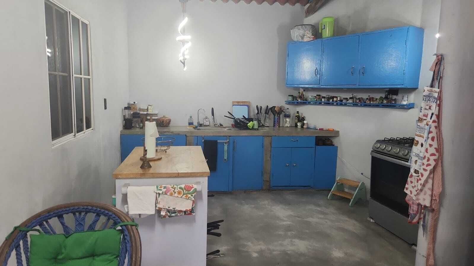 A compact kitchen with blue cabinets, a gas stove, and a small dining area with a chair.