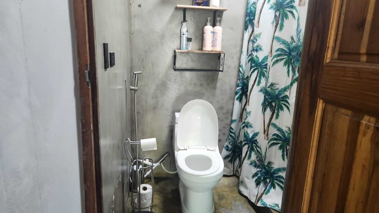 Une petite salle de bain comprenant des toilettes, une douche et une étagère où sont rangés les articles de toilette.