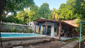 A pool area with a covered patio, surrounded by lush greenery and palm trees. - 3 bedroom Surf and Yoga House (Playa El Tunco)