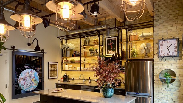 A modern kitchen with a central island, bar stools, a stainless steel refrigerator, and decorative items on shelves. - theLOFTonJAMES, Historic Exchange District, Exposed Brick & Beams, High Ceilings (Winnipeg)