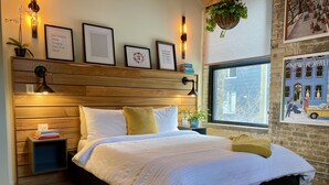 A bedroom with a wooden headboard, a large bed with white bedding, a bedside table with books, and a window with a cityscape view. - theLOFTonJAMES, Historic Exchange District, Exposed Brick & Beams, High Ceilings (Winnipeg)