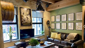 A cozy living room with a brick wall, a large TV, leather sofas, a coffee table, and framed artwork on the wall. - theLOFTonJAMES, Historic Exchange District, Exposed Brick & Beams, High Ceilings (Winnipeg)