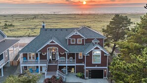 Une maison à deux étages avec un porche à l’avant, un garage et une vue sur l’océan au coucher du soleil.