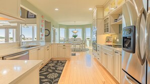 A modern kitchen with a central island, stainless steel appliances, and large windows offering views. - Coral Sunsets & Shimmering Deep Blue Ocean Views! (Ocean Park)