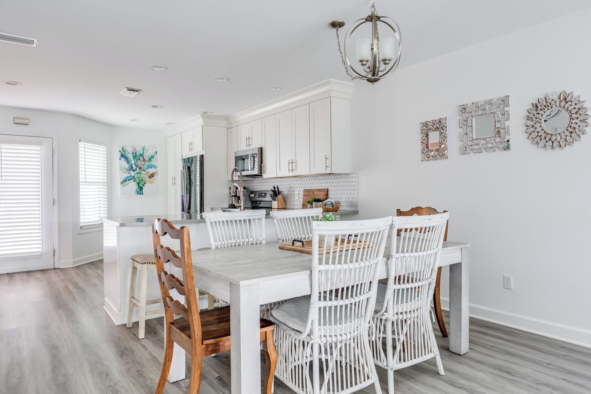 A modern kitchen with white cabinetry, a dining area with white chairs, and a chandelier.