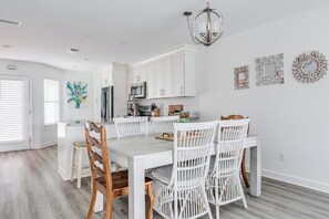 Une cuisine moderne avec des meubles blancs, un coin repas avec des chaises blanches et un lustre.