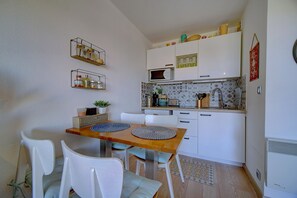 Une cuisine compacte avec des meubles blancs, un four à micro-ondes et un petit coin repas comprenant une table en bois et des chaises blanches.