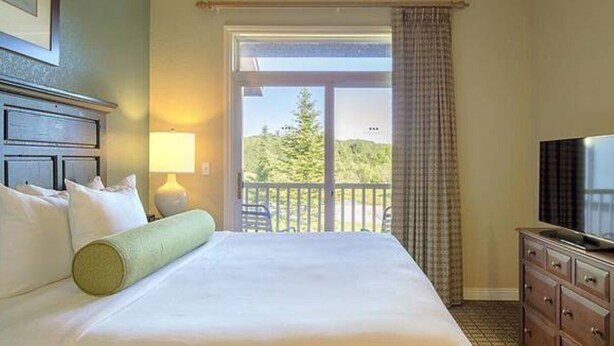 Habitación de hotel con una cama grande, televisor, lámpara y vistas al exterior.
