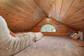 Un dormitorio en el ático, acogedor, con techo inclinado, una ventana con vistas a árboles y una pequeña estantería.