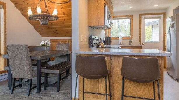 Cocina moderna con armarios de madera, una isla central con taburetes y una zona de comedor con banco y sillas.