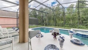 Un espacio al aire libre techado con piscina, sillas de descanso y una mesa lista para comer.