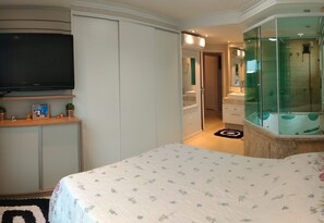 A bedroom with a bed, a television, a wardrobe, and a bathroom with a glass shower enclosure. - High level apartment, air cond. in every room and sea view (Bombinhas)