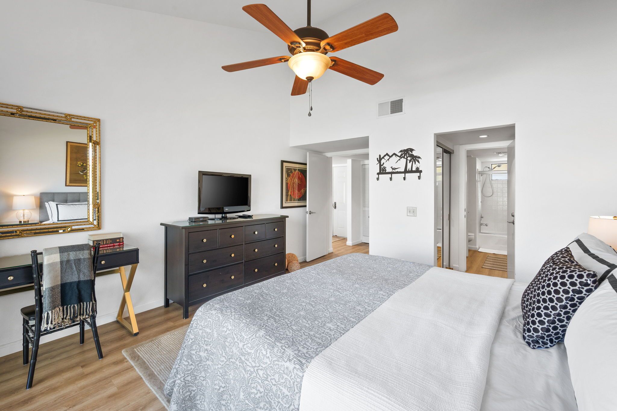 Une chambre à coucher comprenant un lit, un bureau, une télévision, une commode et un ventilateur de plafond.