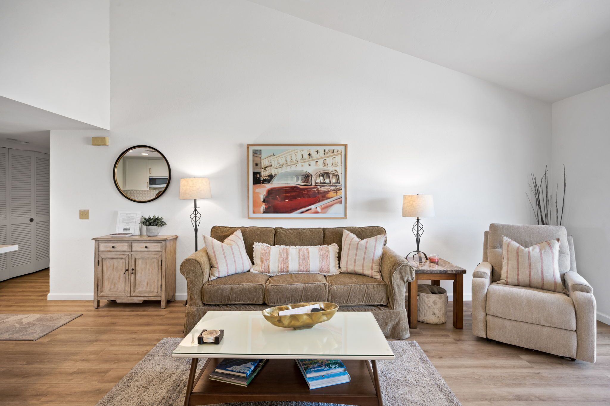 A living room with a sofa, armchair, coffee table, and a painting on the wall.