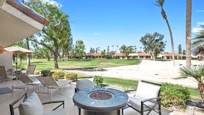 Un espace patio aménagé avec du mobilier d’extérieur, un foyer et une vue sur un terrain de golf.