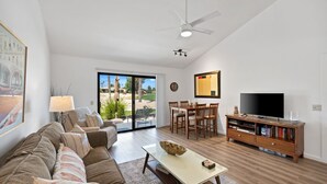 Un salon comprenant un canapé, une table basse, un téléviseur, un meuble de rangement en bois et un coin repas avec des chaises et une table.