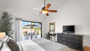Une chambre à coucher avec un lit, une télévision, un bureau et un ventilateur de plafond.