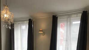 Camera d'albergo con un letto, un lampadario, una lampada a parete e una finestra con tende.