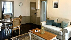 Un soggiorno con tavolo da pranzo apparecchiato, un divano con cuscini, un lampadario e un orologio a parete.