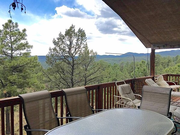 A covered outdoor seating area with wicker chairs and a table, overlooking a mountainous landscape.