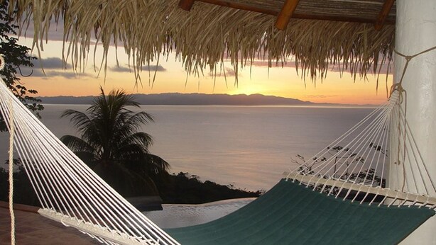 A hammock under a thatched roof overlooking a calm sea at sunset. - Tres Palmas Costa Rica (Puerto Jiménez)