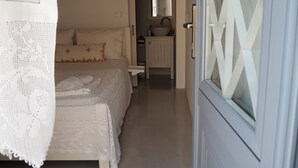 A narrow hallway leading to a bedroom with a bed, a nightstand, a small table, and a mirror.