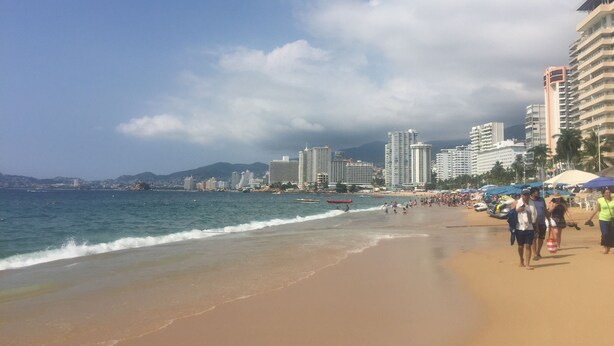 Una spiaggia con uno skyline urbano sullo sfondo, inclusi grattacieli e montagne.