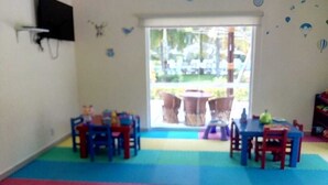 Una stanza con un’area giochi colorata, due tavoli con sedie e un’ampia finestra vista all'esterno.