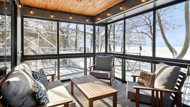 Un espacio interior acogedor con techo de madera, ventanas amplias y vistas a una terraza nevada.