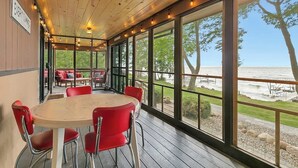 Un espacio comedor techado al aire libre con piso de madera, sillas rojas y grandes ventanales con vista al lago.