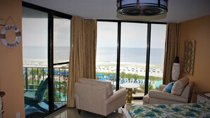 Habitación de hotel con un balcón grande, una cama, un sofá y vista a la playa.
