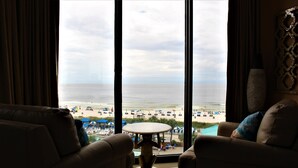 Una habitación con vistas a la playa a través de amplias ventanas, una mesa redonda y dos sillones.