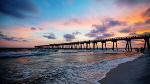Un muelle se adentra en el océano al atardecer, con olas rompiendo contra él.