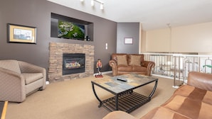 A living room with a fireplace, a sofa, a coffee table, and a television mounted above the fireplace. - Paradise Canyon Golf Resort - Luxury Villa 407 (Lethbridge)