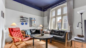Un salón con un sillón rojo, un sofá de cuero negro, una mesa de centro redonda y una ventana con cortinas.