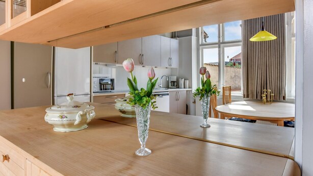 Una cocina moderna con armarios de madera, una mesa de comedor y dos jarrones de vidrio con flores.