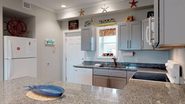 A kitchen with granite countertops, a dishwasher, a stove, and a refrigerator. There are decorative items on the wall and a window with curtains. - Walk to Sandfest, Shared Pools, Boardwalk to Beach (Port Aransas)