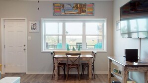 A room with a large window, a wooden table with four chairs, a small TV on a wooden stand, and a door. - Walk to Sandfest, Shared Pools, Boardwalk to Beach (Port Aransas)