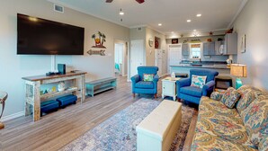 A spacious living room with a flat-screen TV, blue armchairs, a sofa, and a wooden coffee table. - Walk to Sandfest, Shared Pools, Boardwalk to Beach (Port Aransas)