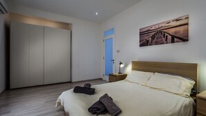 A bedroom with a bed, a nightstand, a lamp, a wardrobe, and a painting on the wall. - Perfectly Located Sliema Apartment (Sliema)